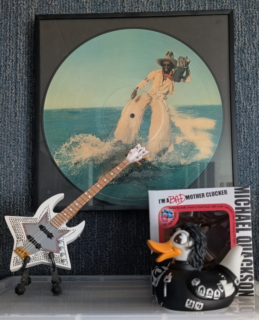 Miniatuur van de iconische Bootsy Collins-sterrenbas naast de humoristische Michael Quackson als onderdeel van Roy's muziekmemorabilia.