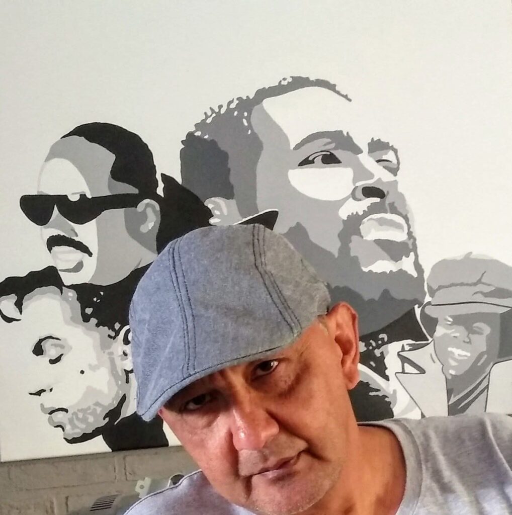 Roy Chamberlain poseert voor een muurschildering met iconische soul- en funkartiesten die zijn muzikale passie weerspiegelt.